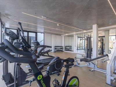 Nowoczesny sprzęt fitness w jasnej, przestronnej siłowni z dużymi oknami.