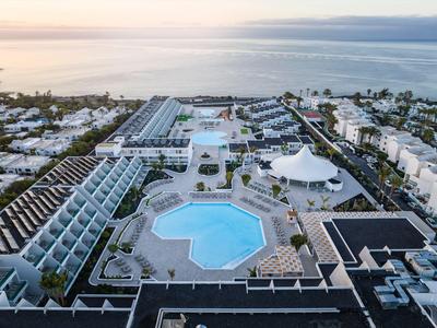 Widok z lotu ptaka na hotel z dużym basenem i widokiem na morze o zachodzie słońca.