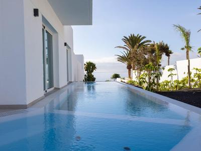 Moderner Außenbereich mit rechteckigem Pool, weißen Wänden, Palmen und blauem Himmel.