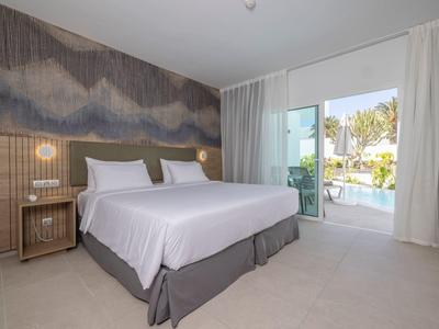 Modernes Schlafzimmer mit Doppelbett, grauem Teppich, Nachttischen und Blick auf Terrasse mit Pool.