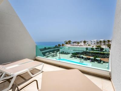 Blick von Balkon mit Liegestühlen auf Pool und Meer im Hotel.