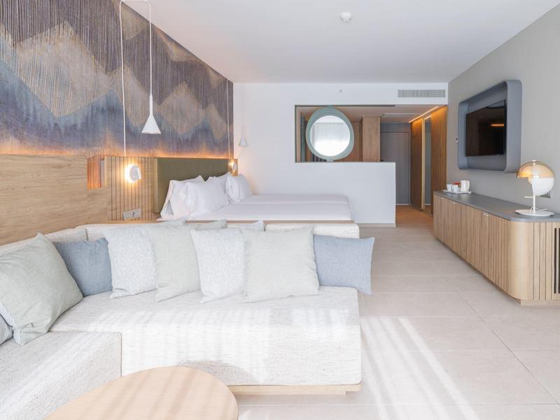 Heller, moderner Wohnraum mit weißem Sofa, Holzmöbeln und offenem Schlafzimmer im Hintergrund.