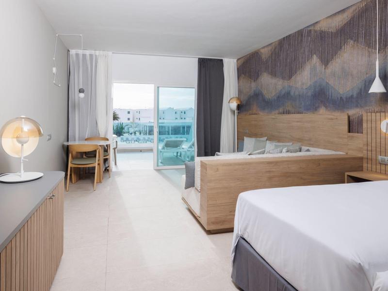 Helles Hotelzimmer mit Bett, Holzverkleidung, Schreibtisch, Balkon und moderner Wandgestaltung.