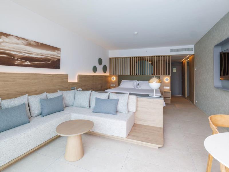 Modern eingerichtetes Lounge-Zimmer mit Sofa, runden Tischen und dekorativen Wandobjekten in neutralen Tönen.