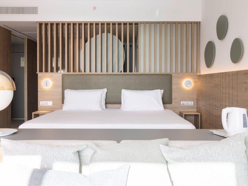 Schlichtes helles Schlafzimmer mit großem Bett, Holzpaneelen, runden Spiegeln und moderner Deko.