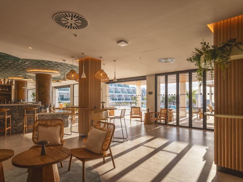 Heller, moderner Gastraum mit Holzsäulen, großen Fenstern und gemütlichen Sitzbereichen.