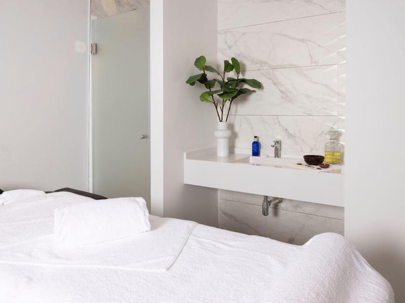 Weißes Schlafzimmer mit Bett, Handtüchern, modernem Waschbecken und Pflanze auf Marmorwand.