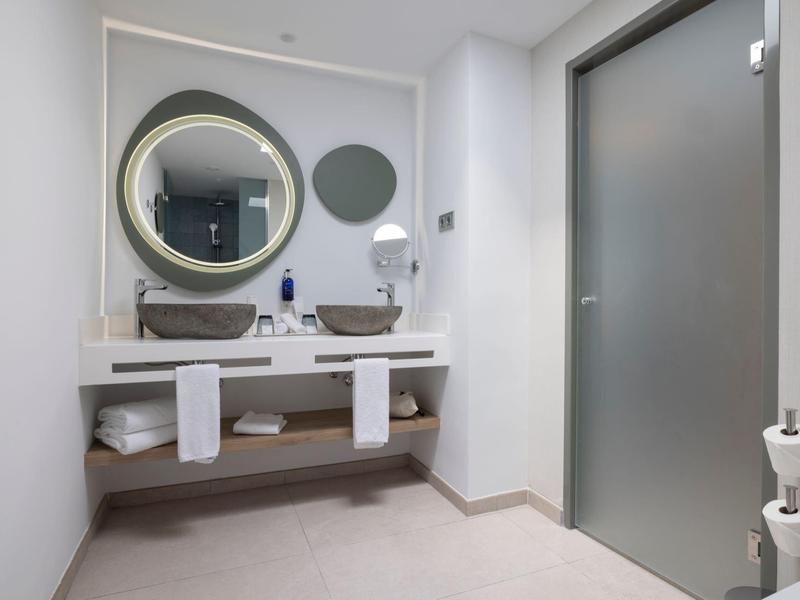 Modernes Badezimmer mit rundem Spiegel, weißem Waschbecken und grauer Glastür.