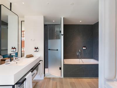 Moderner Badbereich mit weißem Waschbecken, großer Spiegel, Glasdusche und grauer Badewanne.