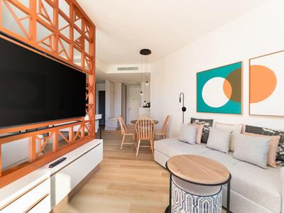 Helles Wohnzimmer mit weißem Sofa, Holzboden, modernen Couchtischen und großer Fernsehwand.