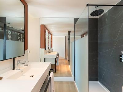 Moderner Badezimmerbereich mit weißen Waschbecken, großen Spiegeln und schwarzer Duschwand.