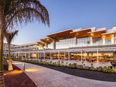 Modernes Gebäude mit großflächigen Glasfenstern, Holzverkleidung und Palmen im Vordergrund.