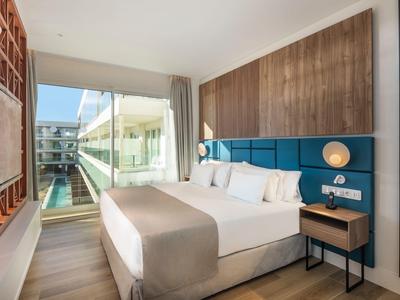 Modernes Hotelzimmer mit großem Bett, Holzakzenten und Blick auf Pool und Gebäude.