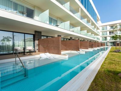 Modern hotel pool with lounge chairs and glass railings in sunny weather.