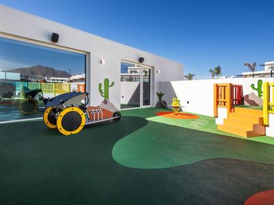 Moderner Kinderspielplatz mit weichem Boden, Tunnelrutsche, Trampolin und Klettergerüst bei Sonnenschein.