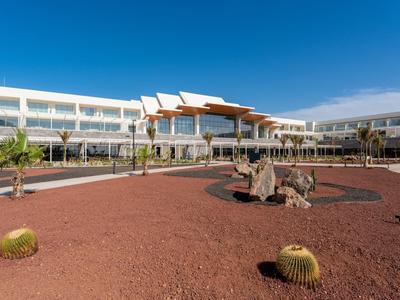 Moderner Hotelkomplex mit weißem Gebäude um roten Kiesgarten und blauem Himmel.