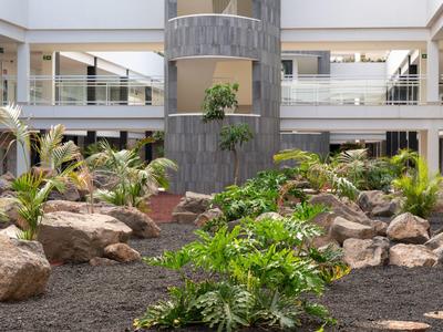 Innenhof mit Pflanzen, großen Steinen und einem mehrstöckigen Gebäude im Hintergrund.