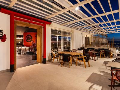 Wieczorny taras restauracji z drewnianymi stołami pod przezroczystym dachem.