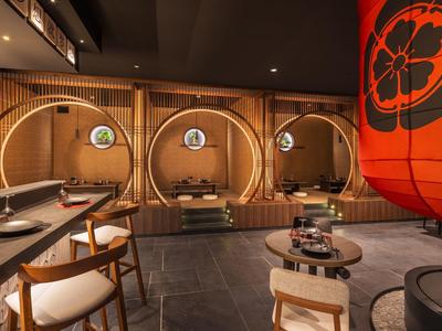Modernes japanisches Restaurant mit runden Holzkabinen, gedeckten Holztischen und großem rotem Lampion.