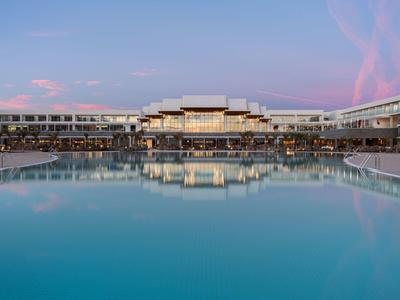 Ein großes modernes Hotel mit langgestrecktem Pool und rosa-blauem Abendhimmel.