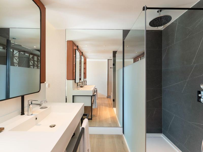 Moderner Badezimmerbereich mit weißen Waschbecken, großen Spiegeln und schwarzer Duschwand.