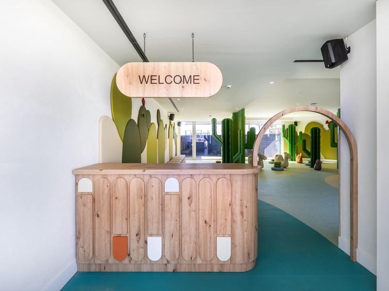 Moderner Empfangsbereich mit hölzerner Rezeption und grünen Pflanzenmotiven in hellen Farben.