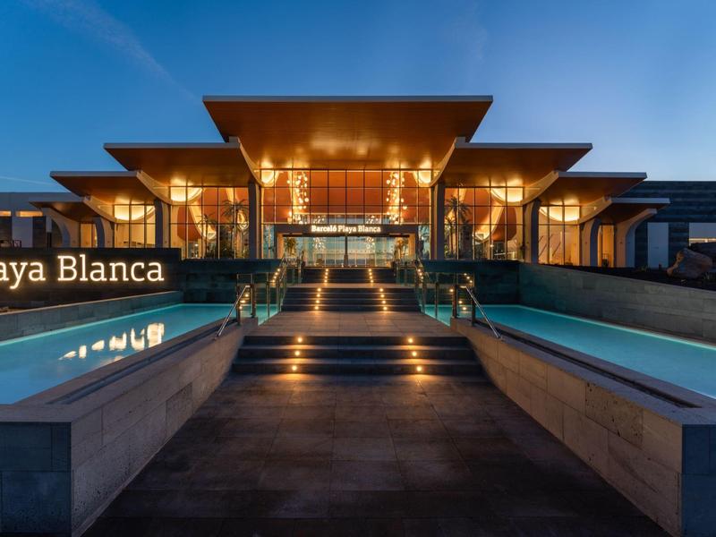 Moderne Villa mit großem Pool bei Sonnenuntergang, klarer Himmel, warmes Licht innen und außen.