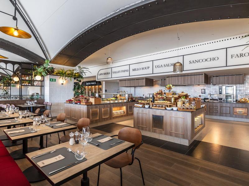 Moderne Restaurantinneneinrichtung mit Holztischen, roten Sitzbänken und großem Buffetbereich.