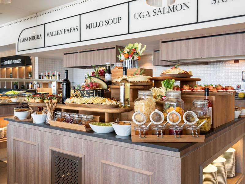 Buffet mit verschiedenen Brotsorten, Frühstücksflocken und Blumenarrangements in modernem Gastraum.