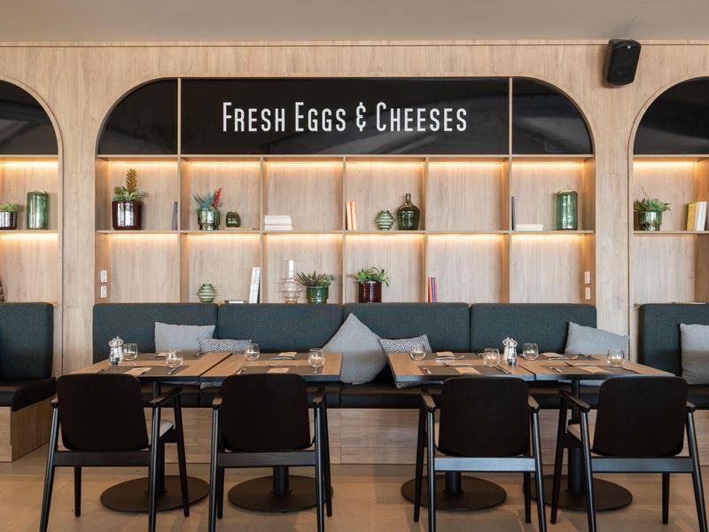 Modernes Restaurant mit Holzwänden und Sitzbänken, beleuchtet, mit Schild 'Fresh Eggs & Cheeses'.