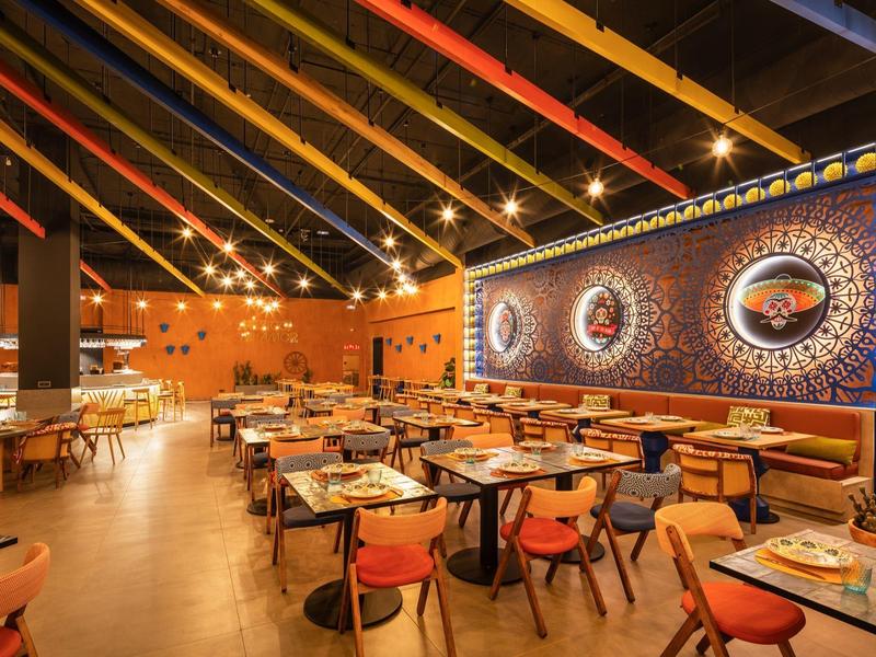 Geräumiges Restaurant mit Holzbalkendecke, warmem Licht, bunten Stühlen und dekorativer Wandgestaltung.