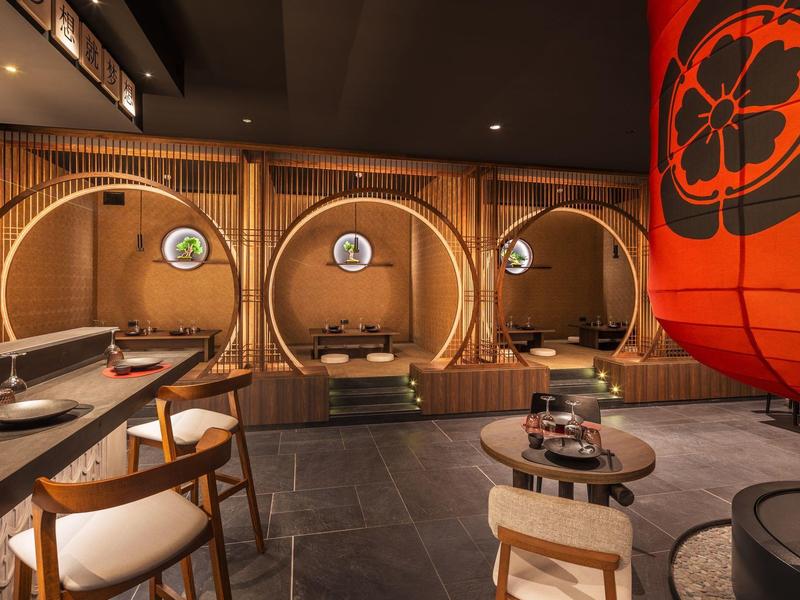 Modernes japanisches Restaurant mit runden Holzkabinen, gedeckten Holztischen und großem rotem Lampion.