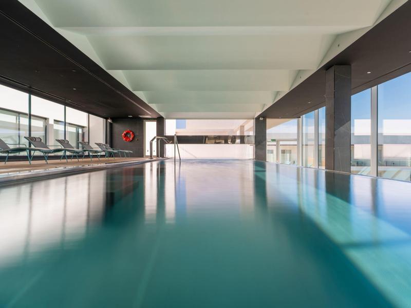 Moderner Hallenbadbereich mit großem rechteckigem Pool und breiten Glasfenstern an beiden Seiten.