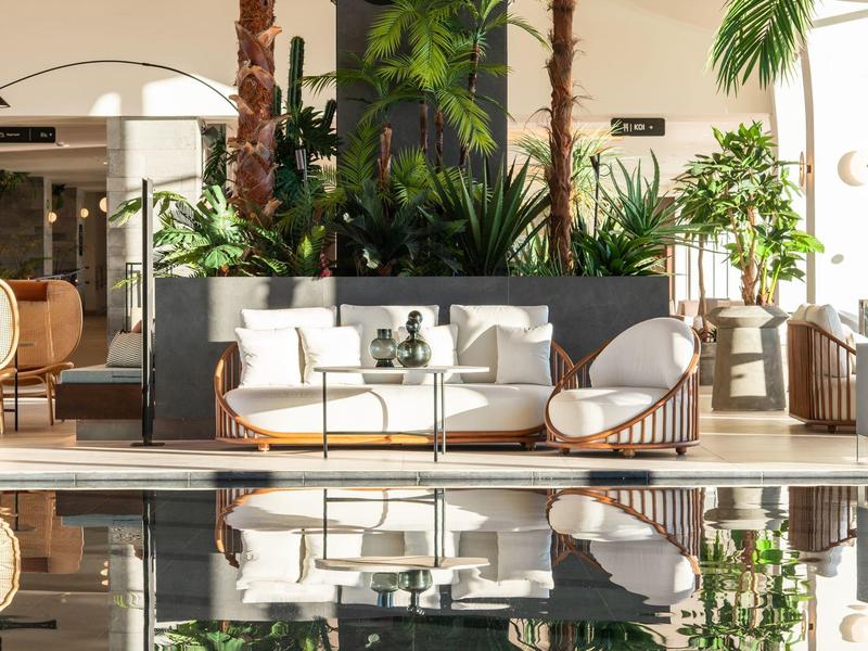Gemütliche Lounge mit weißen Möbeln und Palmen neben einem ruhigen Poolbereich.