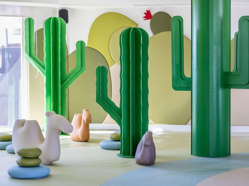 Kinderzimmer mit grünen Kaktus-Skulpturen und weichen Tierfiguren auf dem Boden.