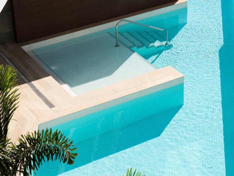 Moderner Außenpool mit klarem Wasser und angrenzendem Whirlpool auf einer Terrasse.