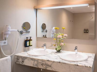 Modernes Badezimmer mit Doppelwaschbecken, großem Spiegel und Blumen in heller, eleganter Atmosphäre.