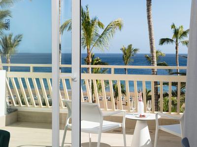 Balkon mit weißen Möbeln, Palmen und Blick auf das blaue Meer unter klarem Himmel.