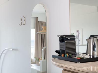 Moderner Küchenbereich mit Kaffeemaschine, Wasserkocher auf Holzarbeitsplatte, Spiegel und Haken an weißer Wand.