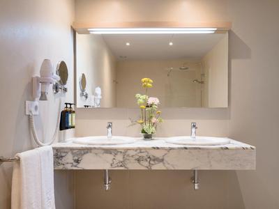 Elegantes Badezimmer mit großem Spiegel, Doppelwaschbecken aus Marmor und frischen Blumen.