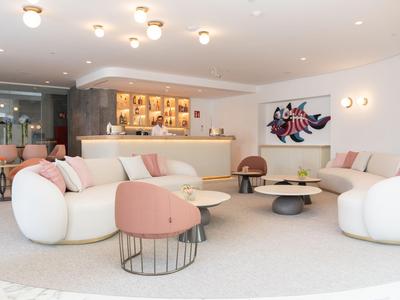 Moderne hotellounge met witte sofa's, roze stoelen en een bar op de achtergrond.