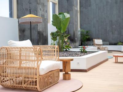 Moderne buitenruimte met rotan fauteuil, houten bijzettafel en parasol op lichte vloertegels.