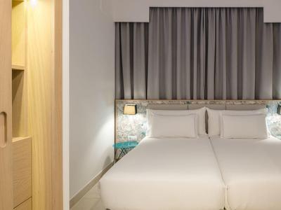 Modernes Hotelzimmer mit zwei Einzelbetten, grauem Vorhang und Holzschrank an der Wand.