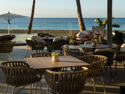 Terrassenmöbel aus Holz und Rattan mit Meerblick bei Sonnenuntergang und Palmen im Hintergrund.