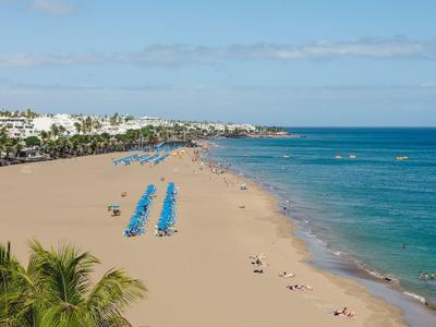 Breid zandstrand met blauwe ligstoelen en turquoise zee onder een blauwe lucht.