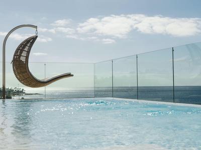 Modernt zwembad met glazen balustrade en hangende rotan stoel met uitzicht op zee.