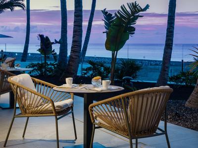 Avondterras met stoelen en tafel met uitzicht op zee en palmbomen.