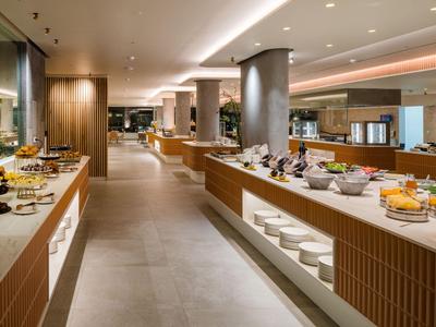 Modern hotelbuffet met diverse gerechten op lange witte balies in een lichte ruimte.