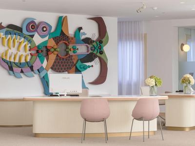 Moderne ontvangstbalie met kleurrijke wandkunst en twee roze stoelen voor een witte balie