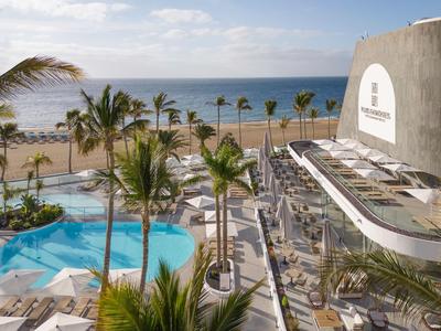 Uitzicht op hotelzwembad met palmbomen en strand op de achtergrond onder een blauwe lucht.